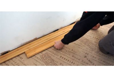 Person installing bamboo flooring against wall